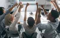 a group of people sitting at a table raising their hands