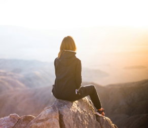 person sitting on top of gray rock overlooking mountain during daytime